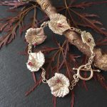 A vine leaf bracelet from the Nature collection, resting on a leaf and branch